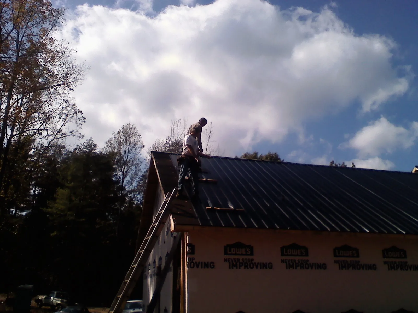 Roofer fastening dark metal panels high against a cloudy sky, from a Roof Inspection job in Ravensdale
