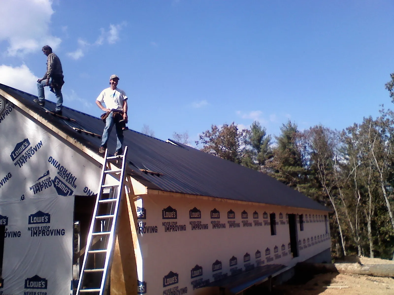 Two roofers standing on a long dark metal roof over a wrapped building in Ravensdale