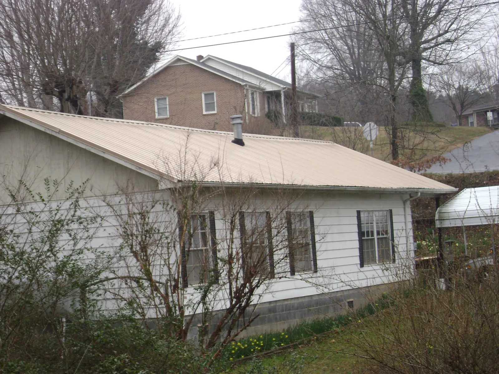 Tan metal roof on a white sided house set into a hillside — Commercial Roofing by Roofing Brothers in Ravensdale
